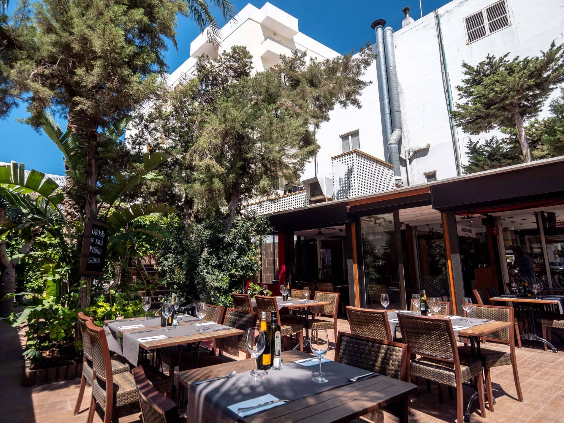 Terraza-jardín de Zebra, con mesas entre árboles y palmeras en Sant Antoni